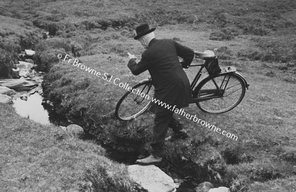 MAN CROSSING STREAM CARRYING BICYCLE